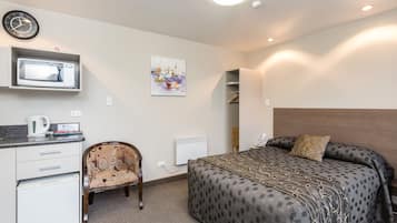 Une chambre d’hôtel avec un lit, une chaise, un bureau avec un micro-ondes, une horloge et un tableau au mur.