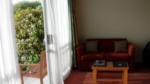 A living room with a red sofa, a wooden coffee table, and a sliding glass door leading to a balcony. - Comfort Inn Tayesta (Invercargill)