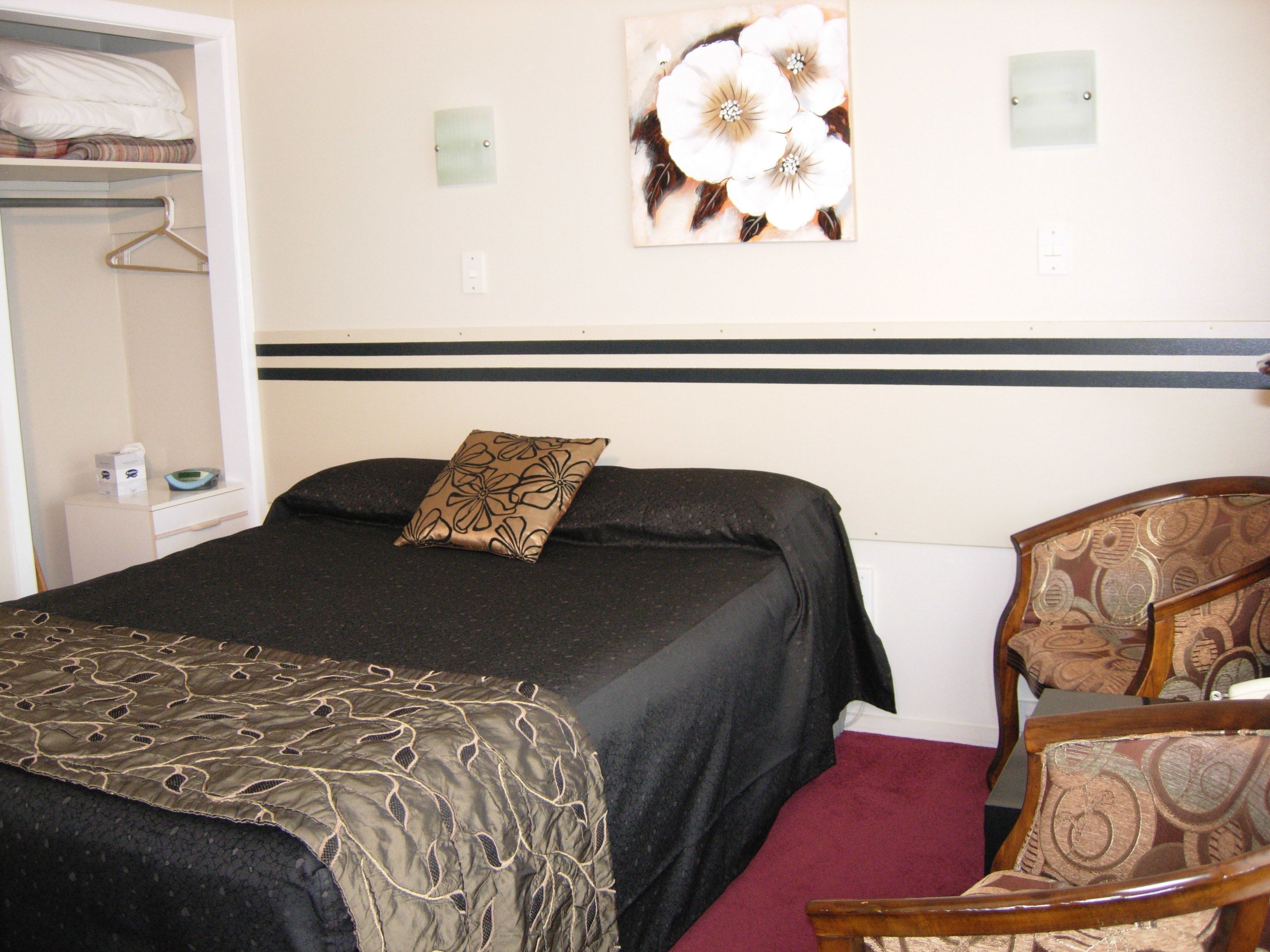 Una habitación de hotel con cama, una silla, un armario y una obra de arte colgada en la pared.
