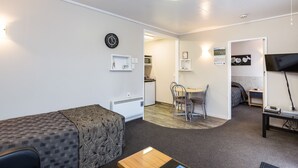 A compact hotel room with a single bed, a small desk, a chair, a television, and a kitchenette. - Comfort Inn Tayesta (Invercargill)