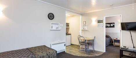 A compact hotel room with a single bed, a small desk, a chair, a television, and a kitchenette.