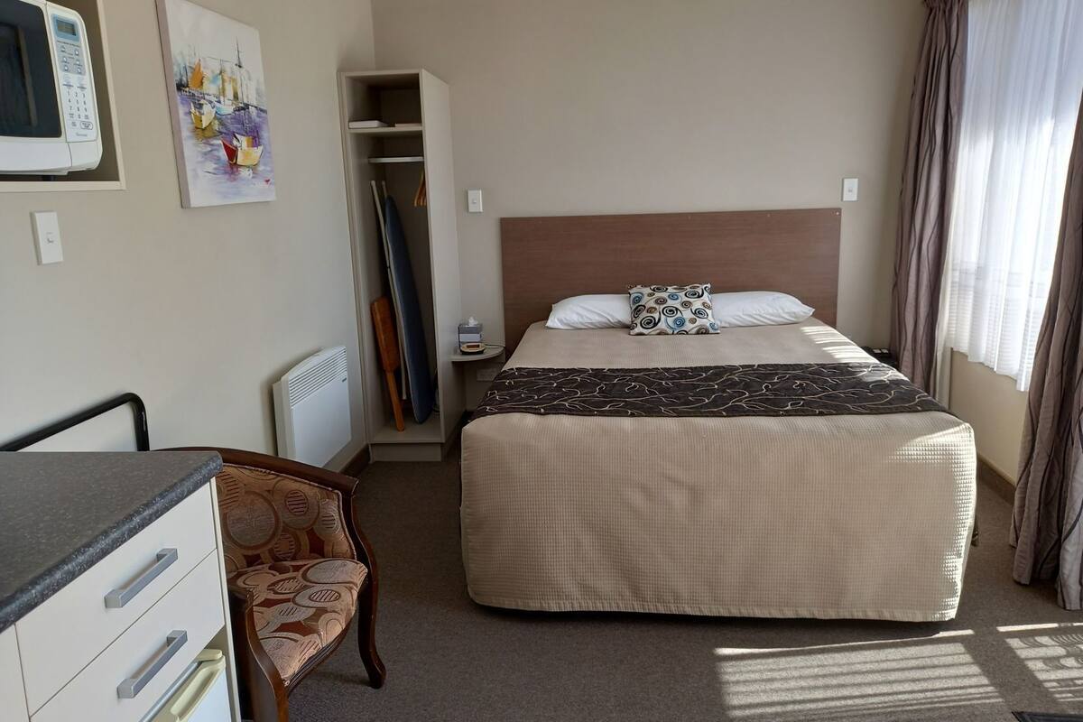 A hotel room with a bed, a desk, a chair, a wardrobe, and a painting on the wall.