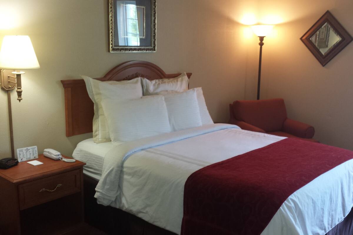 A hotel room with a bed, a nightstand, a lamp, a chair, and a mirror on the wall.