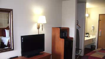 Ein Hotelzimmer mit Fernseher auf einem Holzständer, einer Wandlampe, einer Mikrowelle und einem kleinen Schreibtisch mit Spiegel.