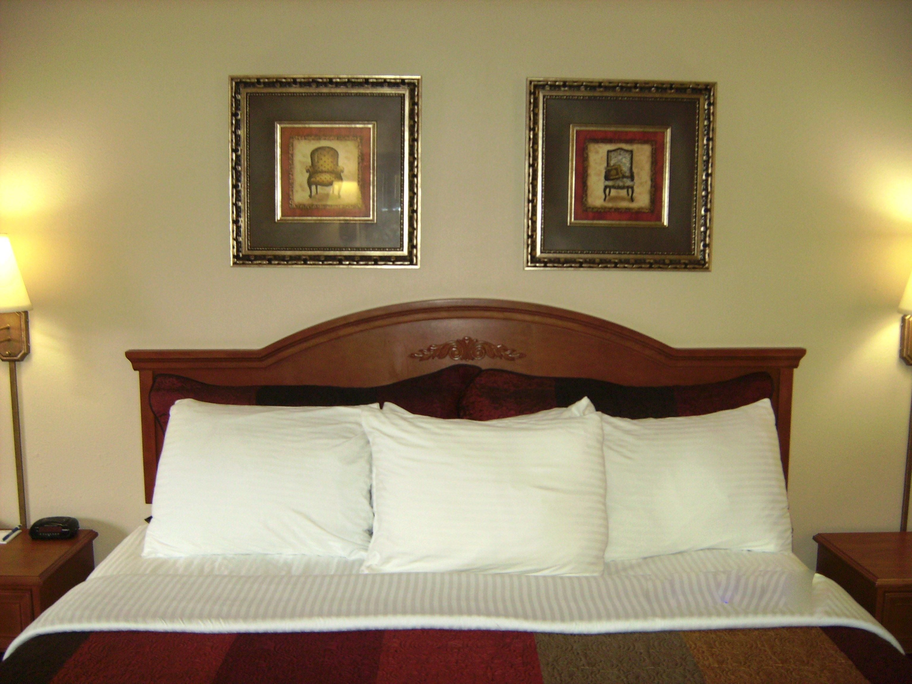 Un lit bien fait, avec des draps blancs et une couverture à rayures rouges et marron. Deux tableaux encadrés sont accrochés au mur au-dessus du lit.