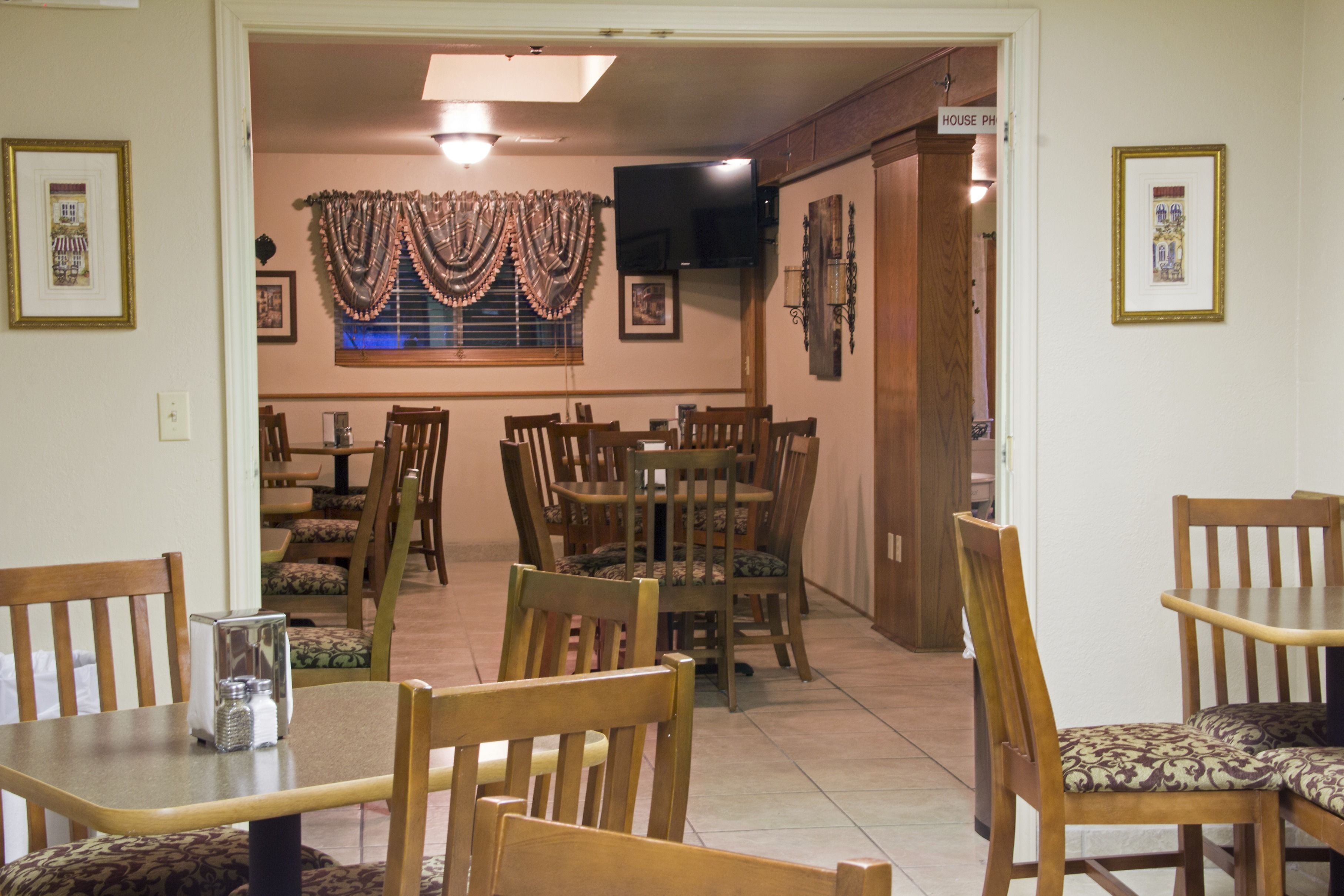 A dining area with wooden tables and chairs, a television mounted on the wall, and a sign indicating the room as 'House PH'.