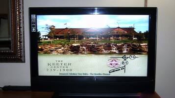 A television displaying a scenic view of a building with a sign reading "The Keeter Center 239-1900".