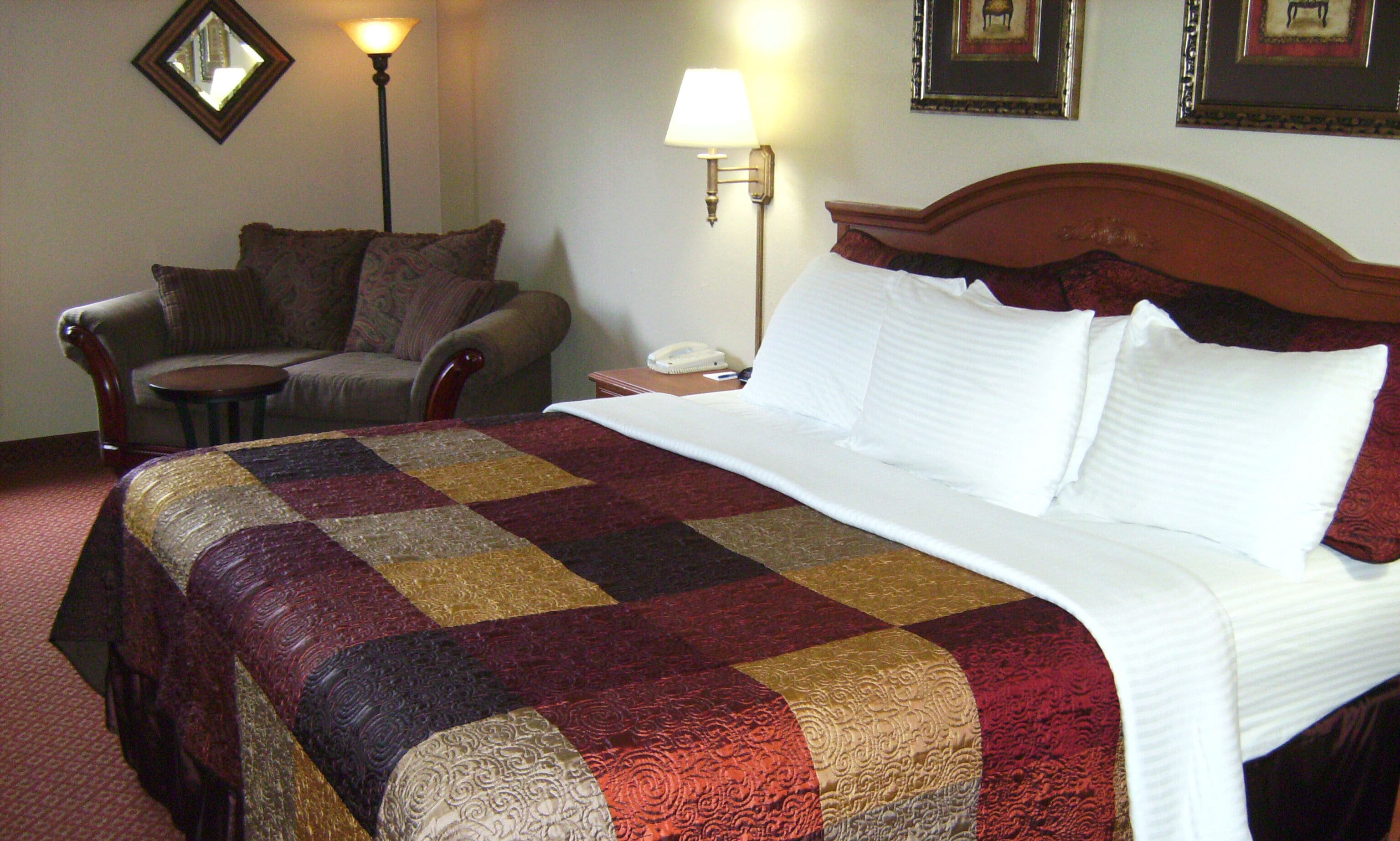 Una habitación de hotel con una cama grande, una silla, una mesita de noche con lámpara y teléfono.