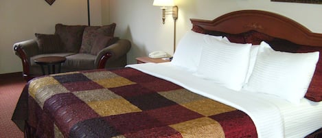 A hotel room with a large bed, a chair, a nightstand with a lamp, and a phone.