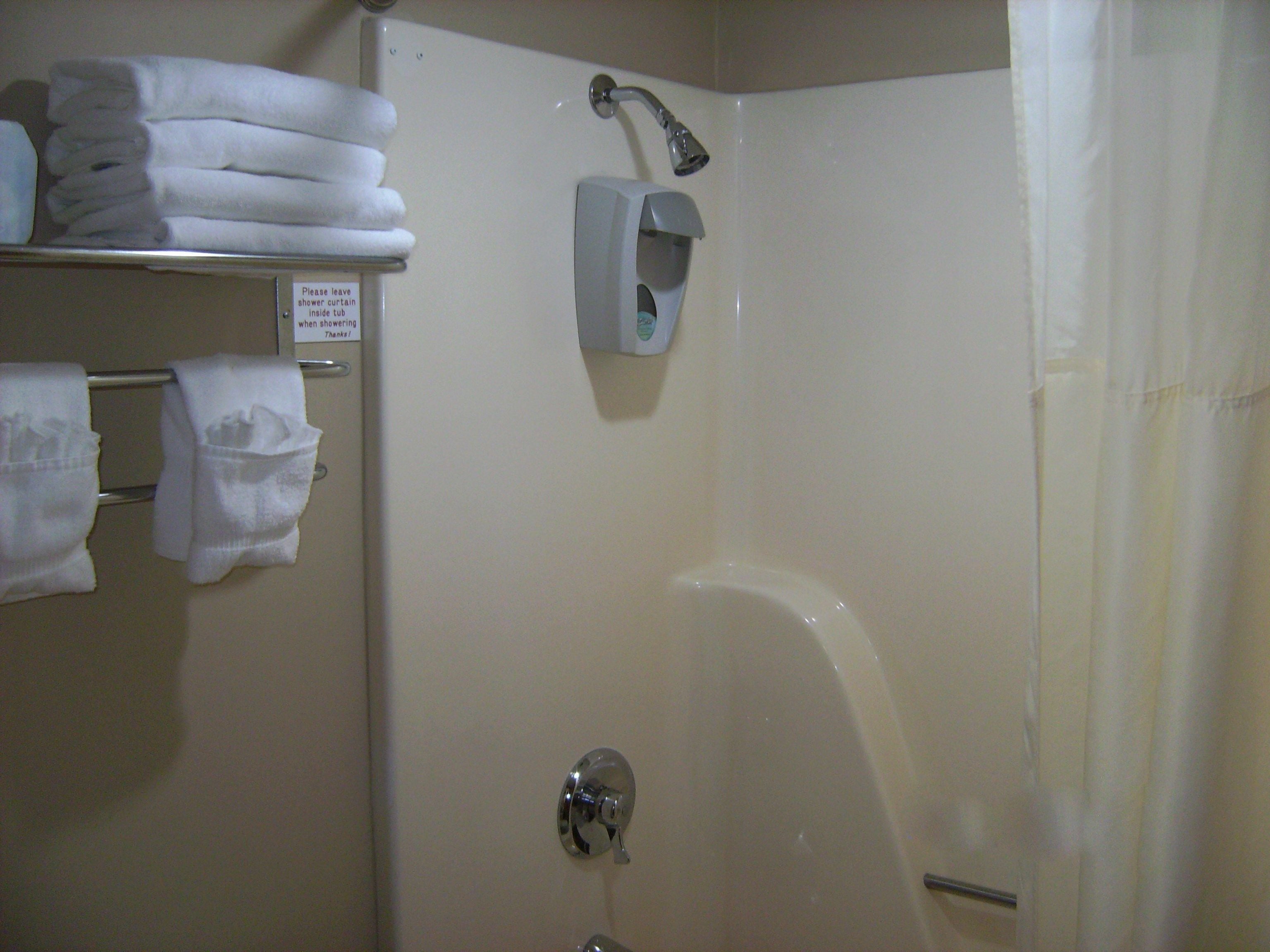 A bathroom with a shower, a towel rack with folded towels, and a sign instructing to leave the shower curtain inside the tub when showering.