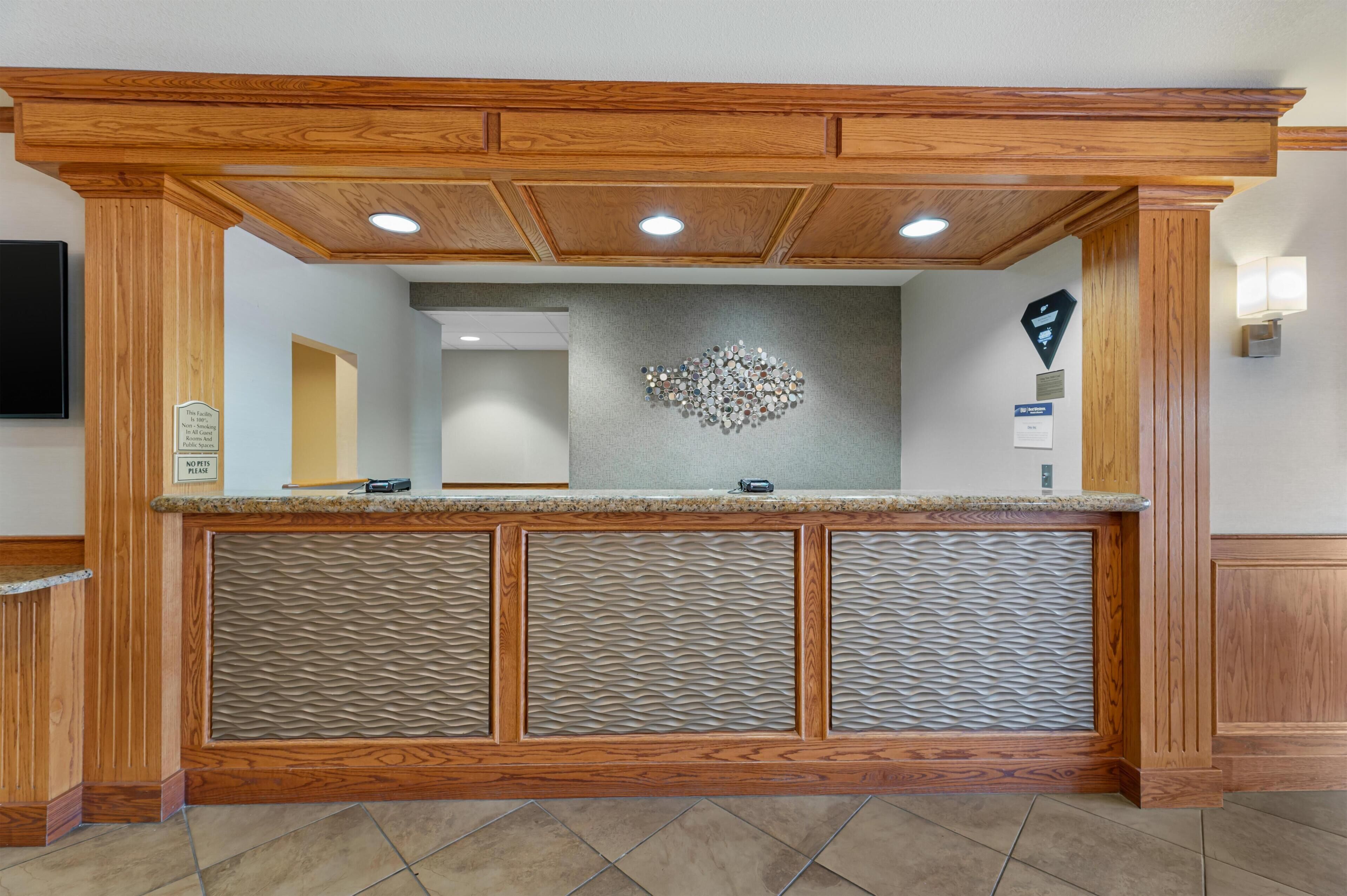 Una reception con piano di lavoro in legno, una parete strutturata sopra e una telecamera di sicurezza a muro.