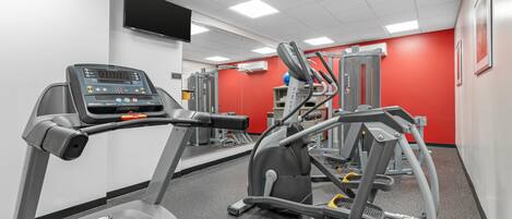 A gym with treadmills, weight machines, and a TV on the wall.