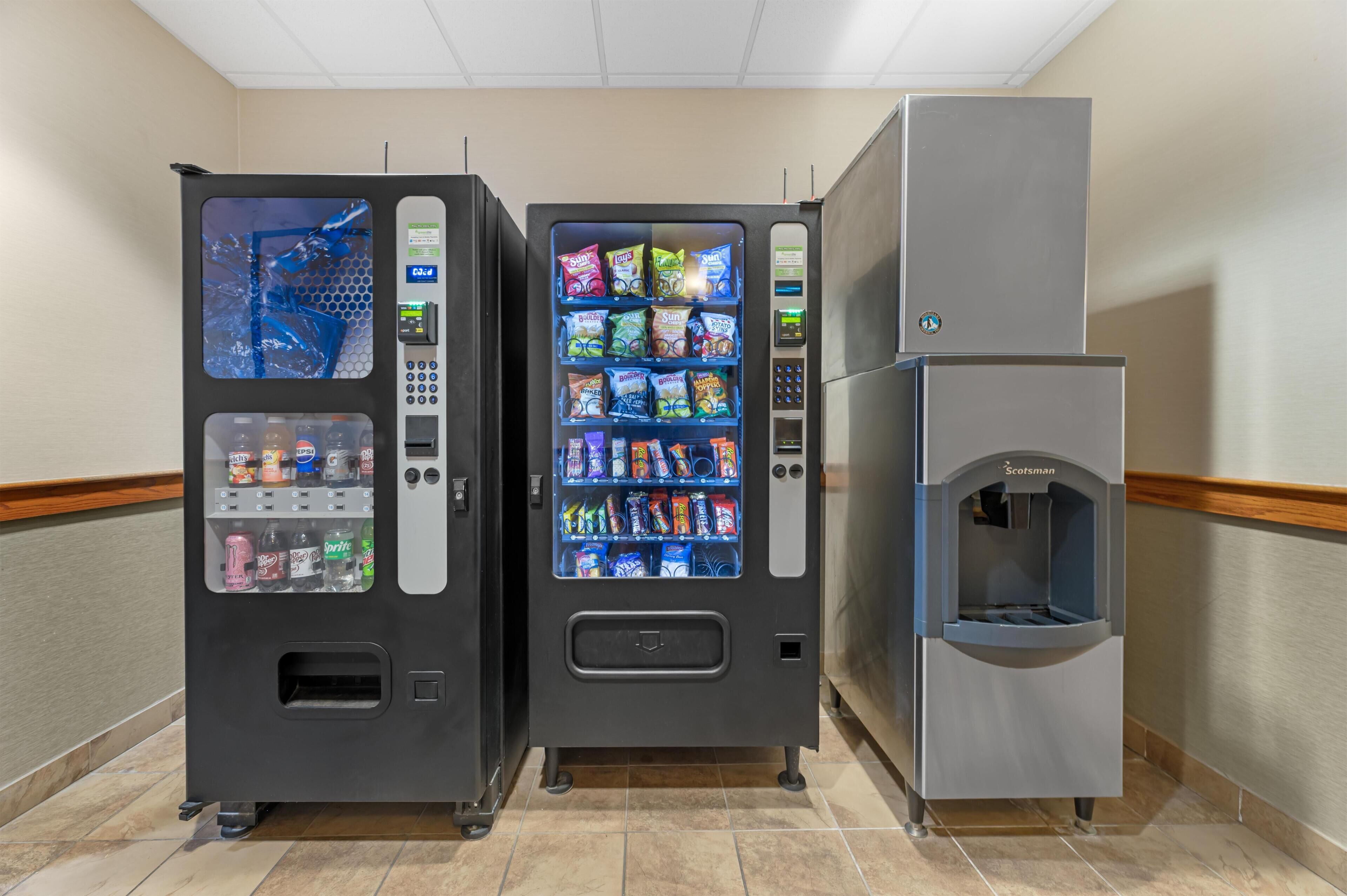 Ein Getränkeautomat mit Snacks und Getränken, ein Wasserspender und eine Kaffeemaschine in einem Flur.