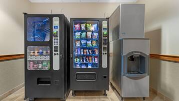 Máquina expendedora con aperitivos y bebidas, dispensador de agua y máquina de café en un pasillo.