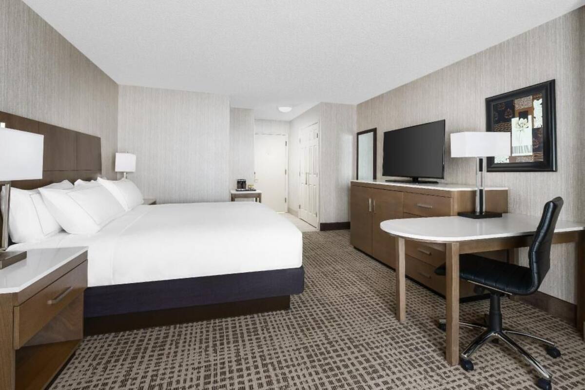 A hotel room with a bed, desk, chair, television, and a wardrobe.