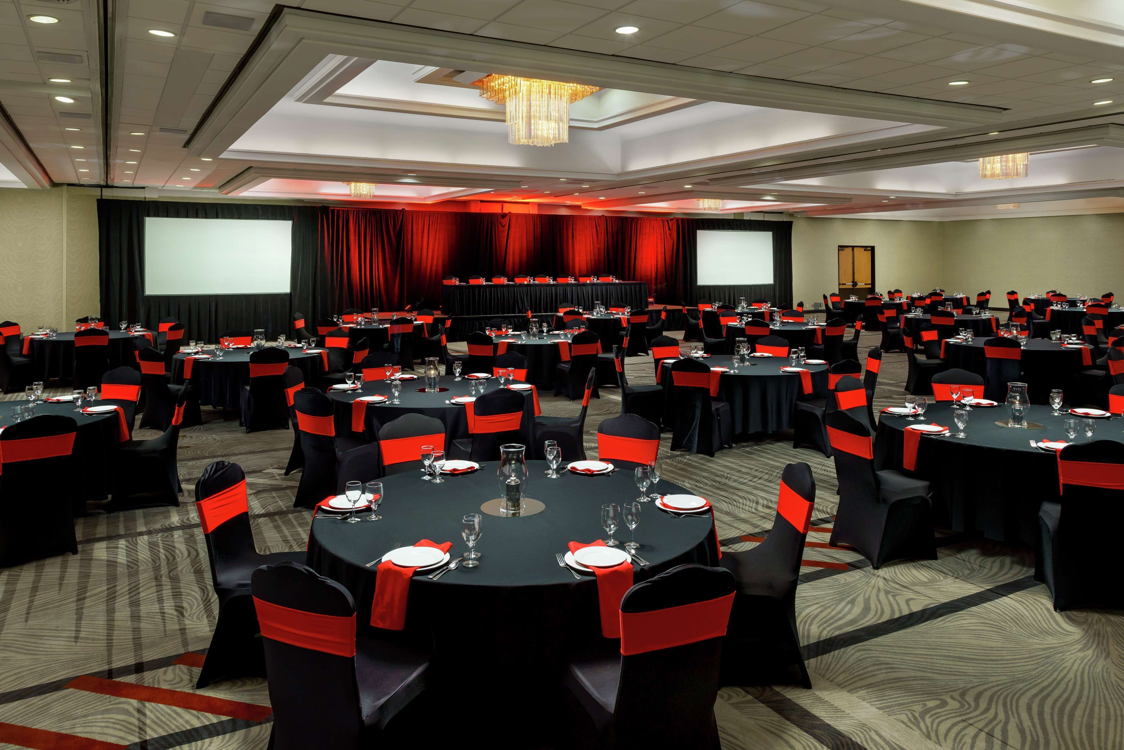 A conference room with multiple round tables, black tablecloths, and red sashes on chairs.