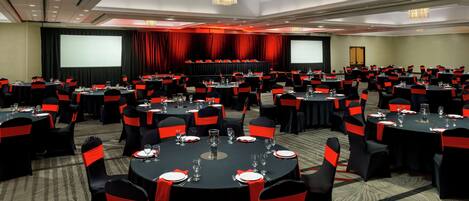 A conference room with multiple round tables, black tablecloths, and red sashes on chairs.
