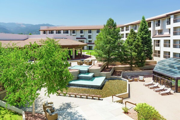 A hotel courtyard with a pool, lounge chairs, and a covered seating area.