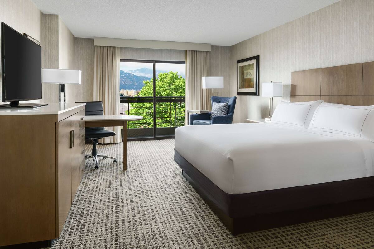 A hotel room with a large bed, a desk with a computer, a chair, and a TV.