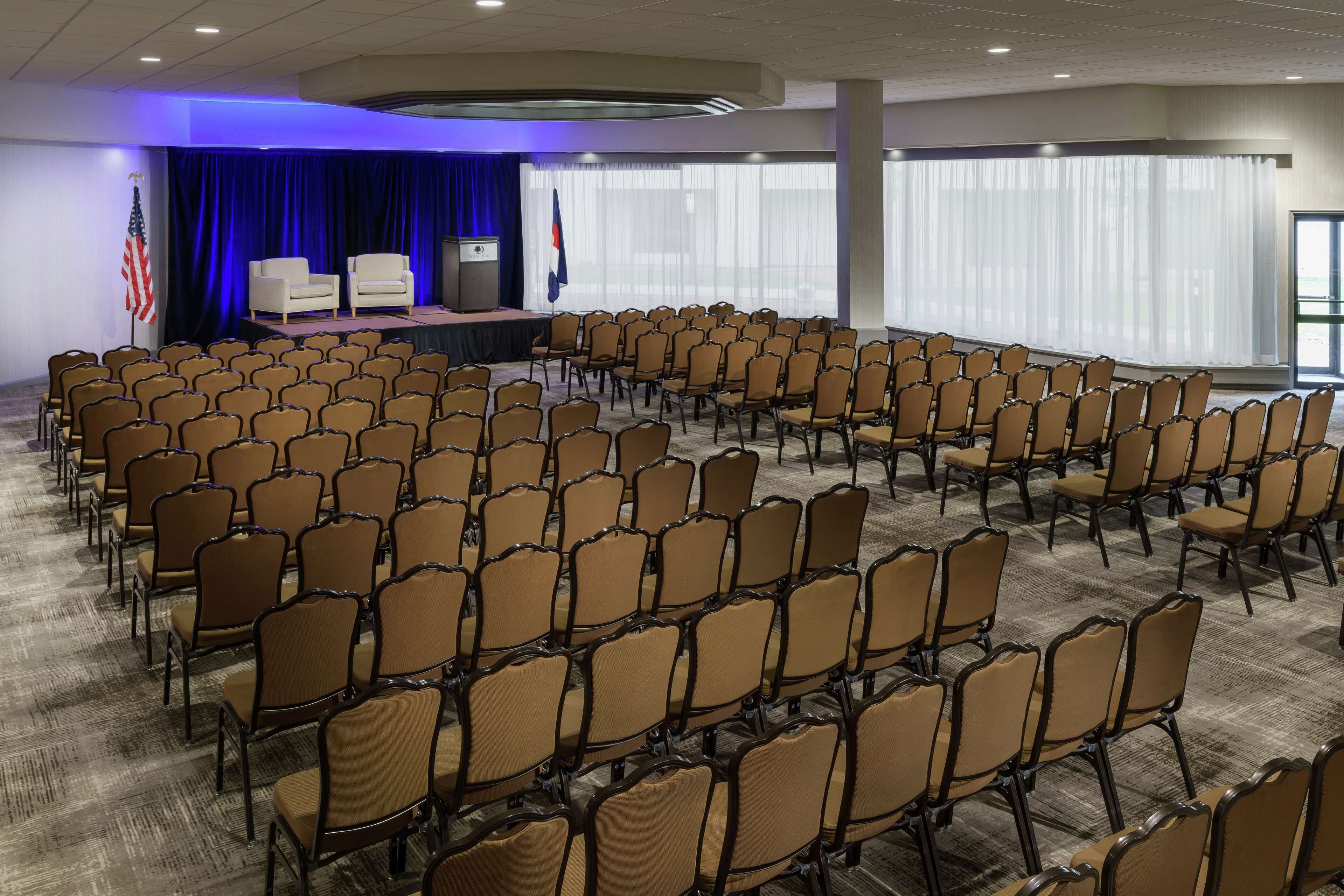 A conference room with rows of chairs, a stage with a podium, and flags.