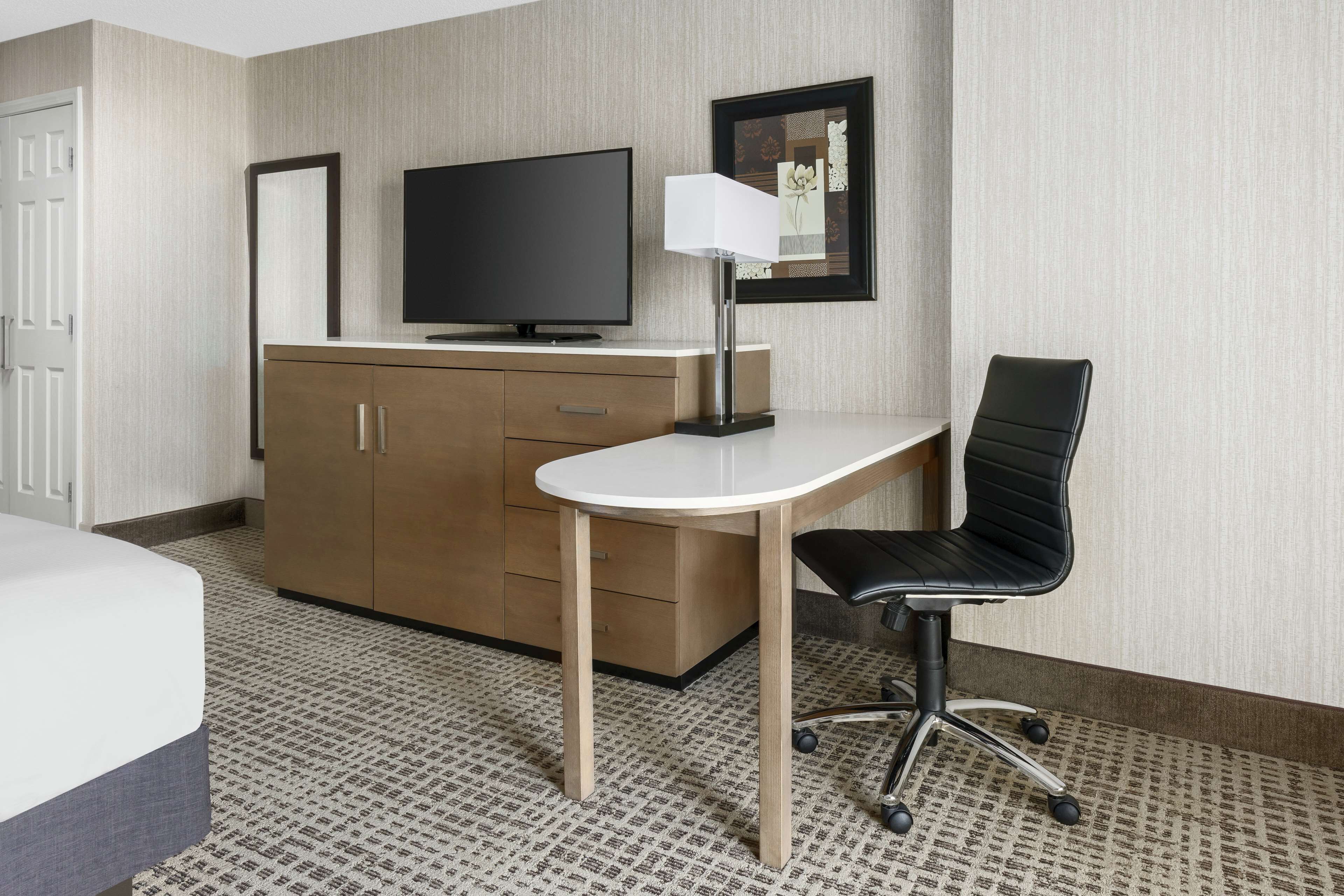 Una habitación de hotel con una cama, un escritorio con una silla, un televisor y un armario.