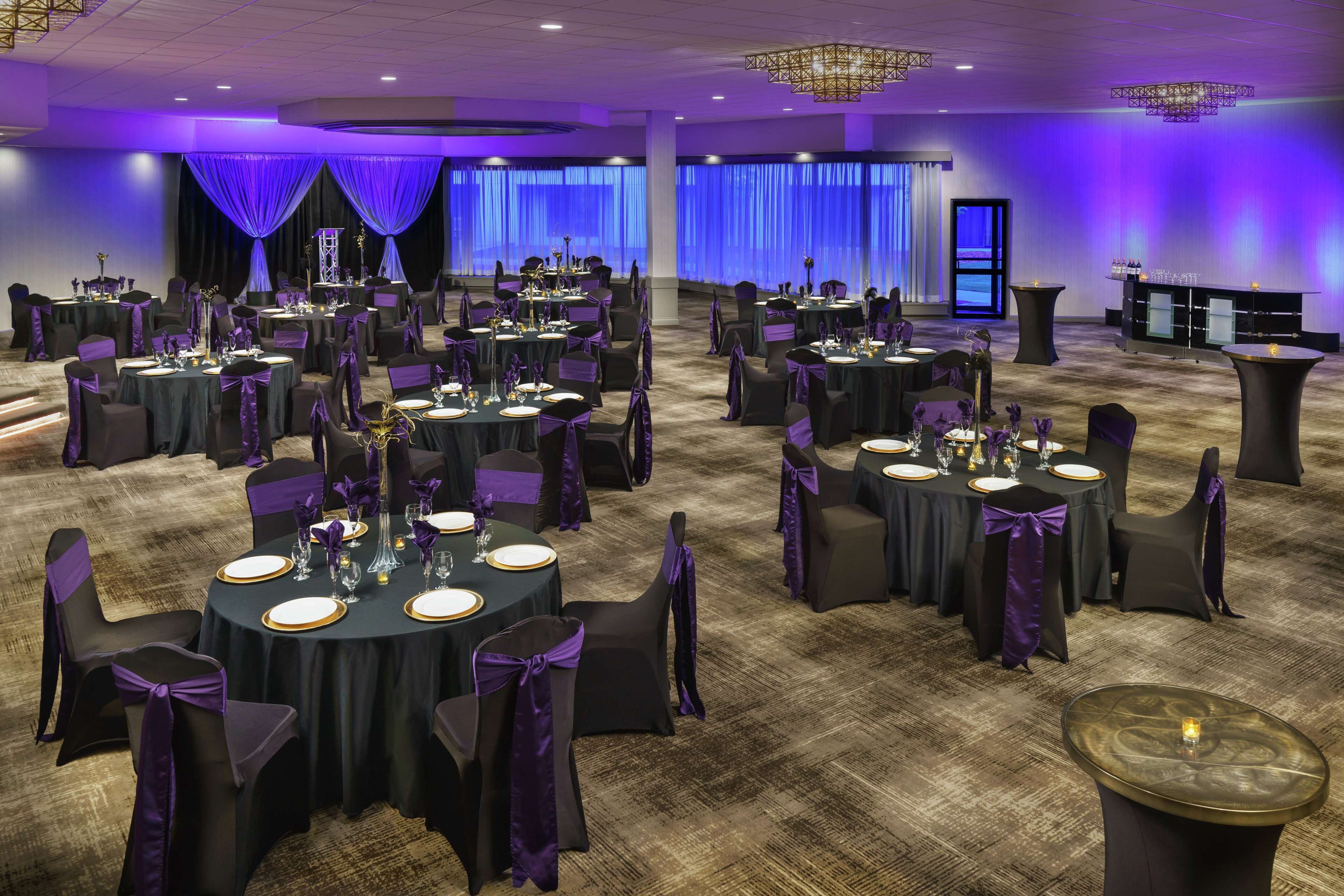 A banquet hall with round tables, chairs, and purple decorations.