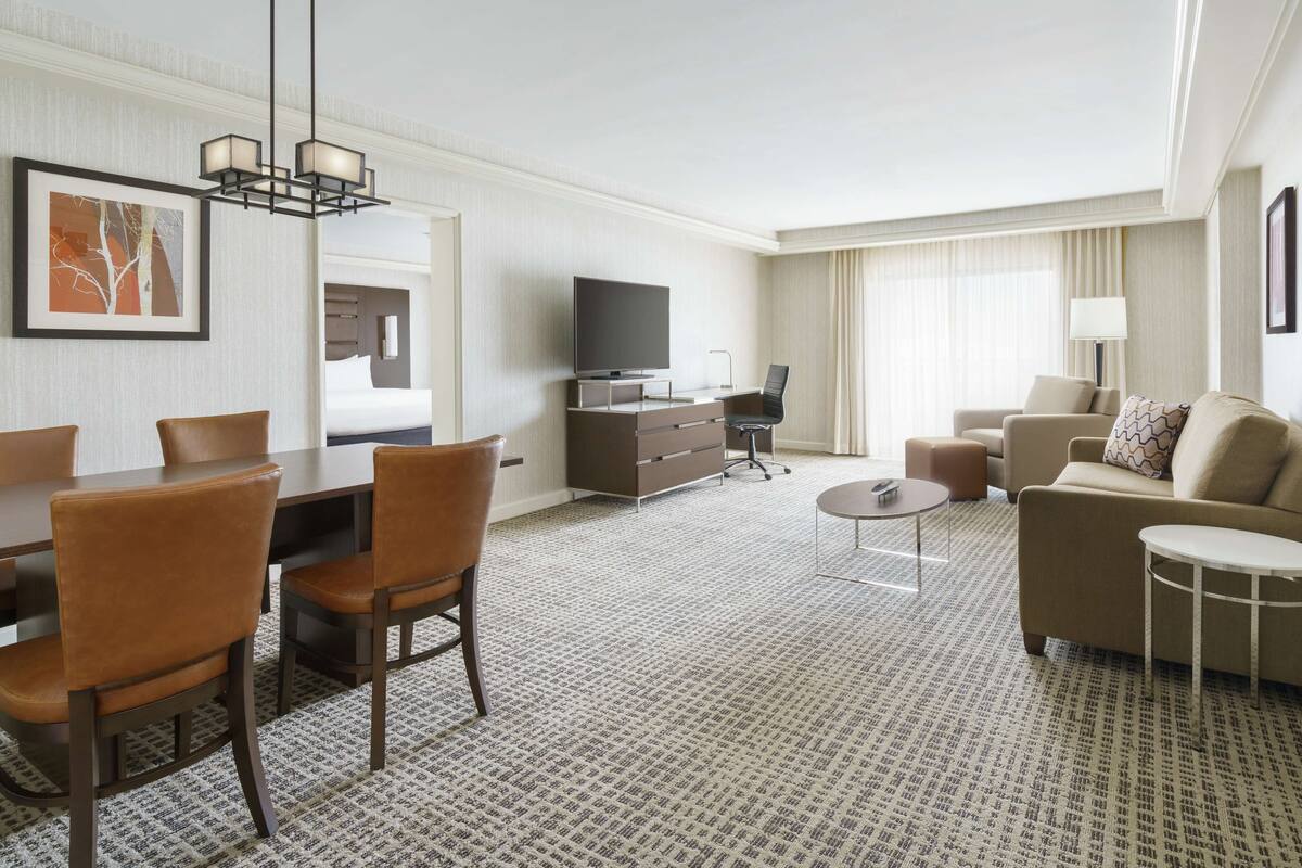 A hotel room with a dining area, a sofa, a TV, and a bed.