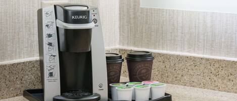 A Keurig coffee maker with a drip tray and several disposable coffee cups.