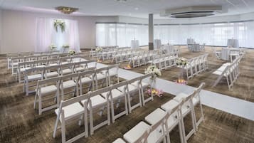 Amplio y bien iluminado salón con filas de sillas blancas dispuestas para un evento.