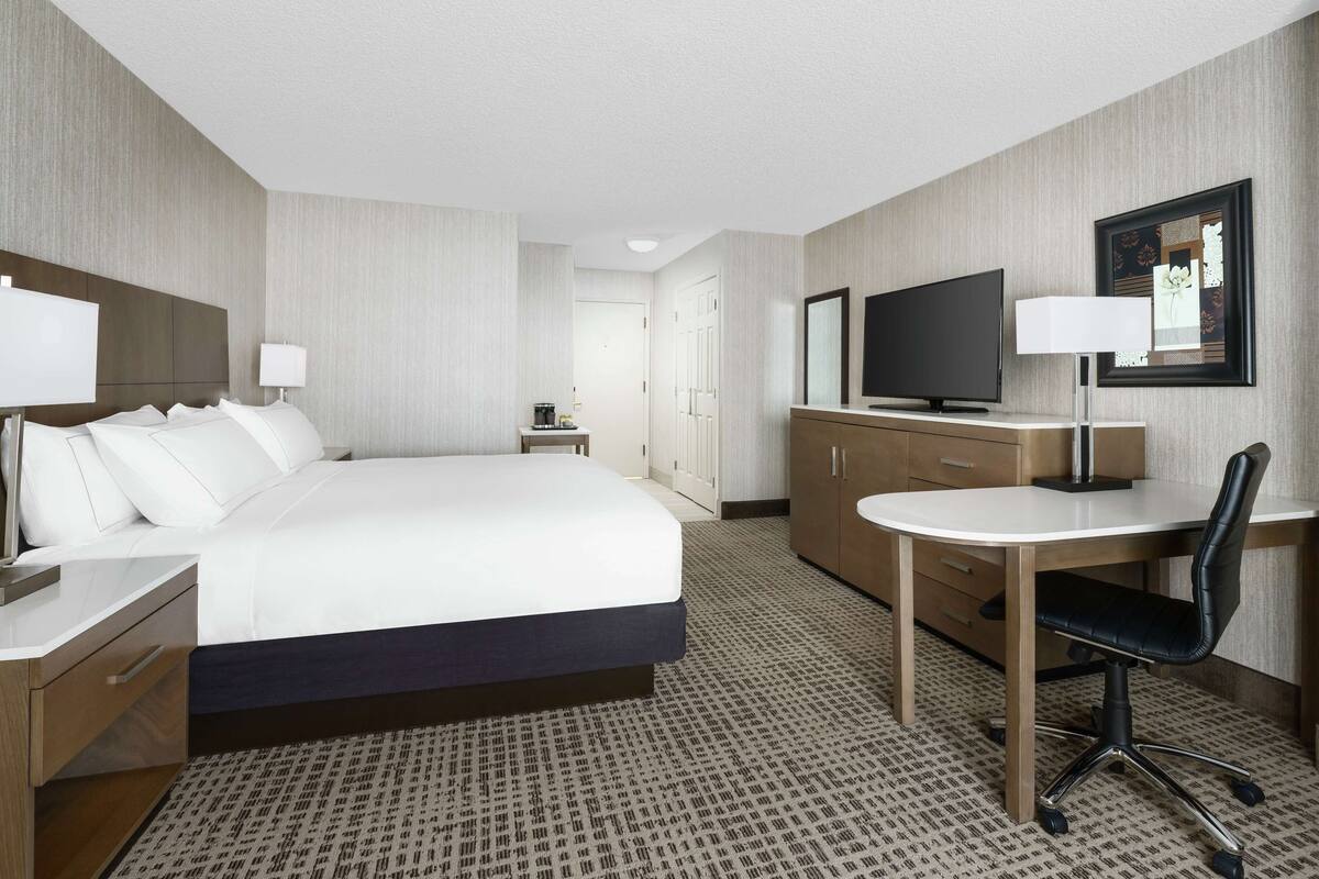 A hotel room with a large bed, a desk with a chair, a television, and a wardrobe.