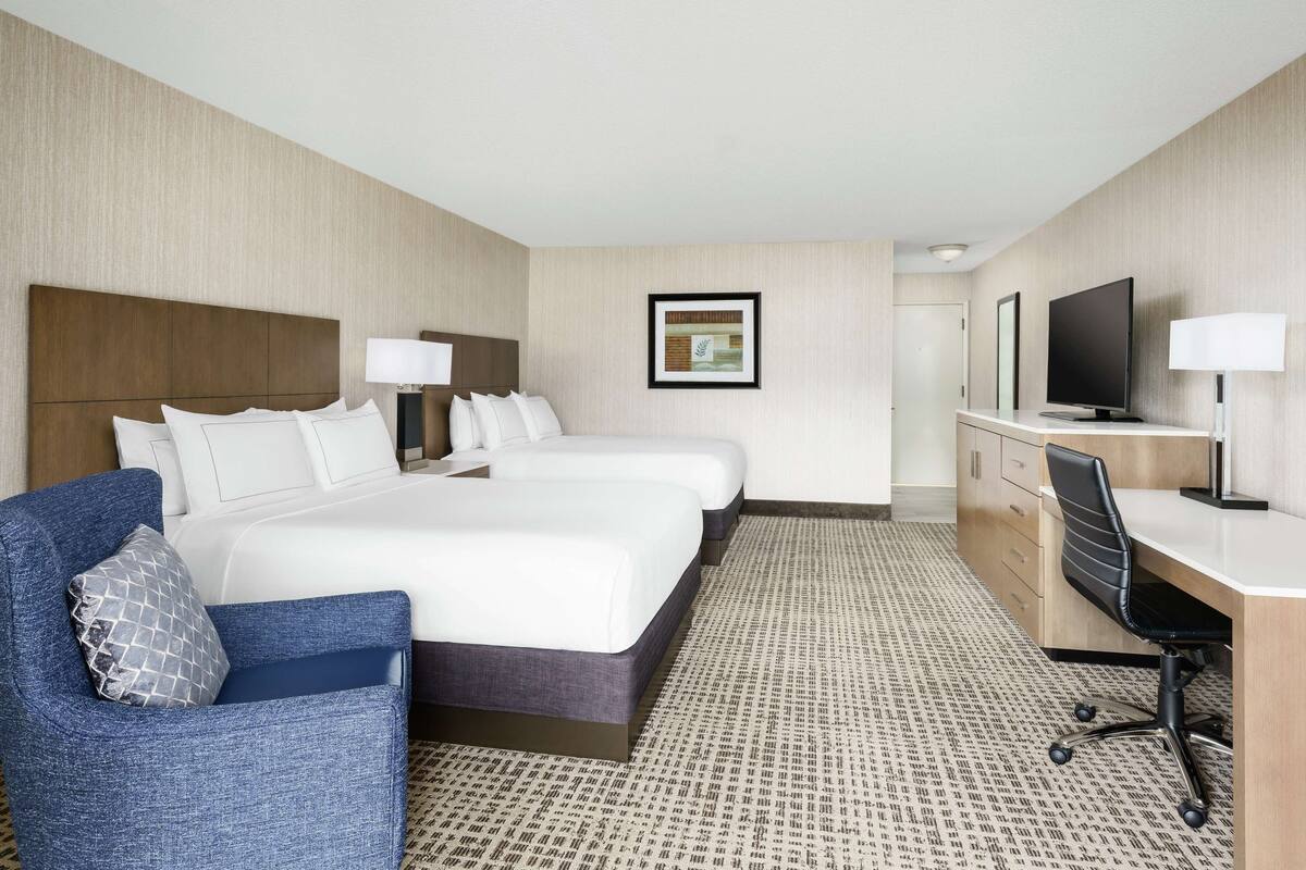 A hotel room with two beds, a desk, a chair, a television, and a framed picture on the wall.