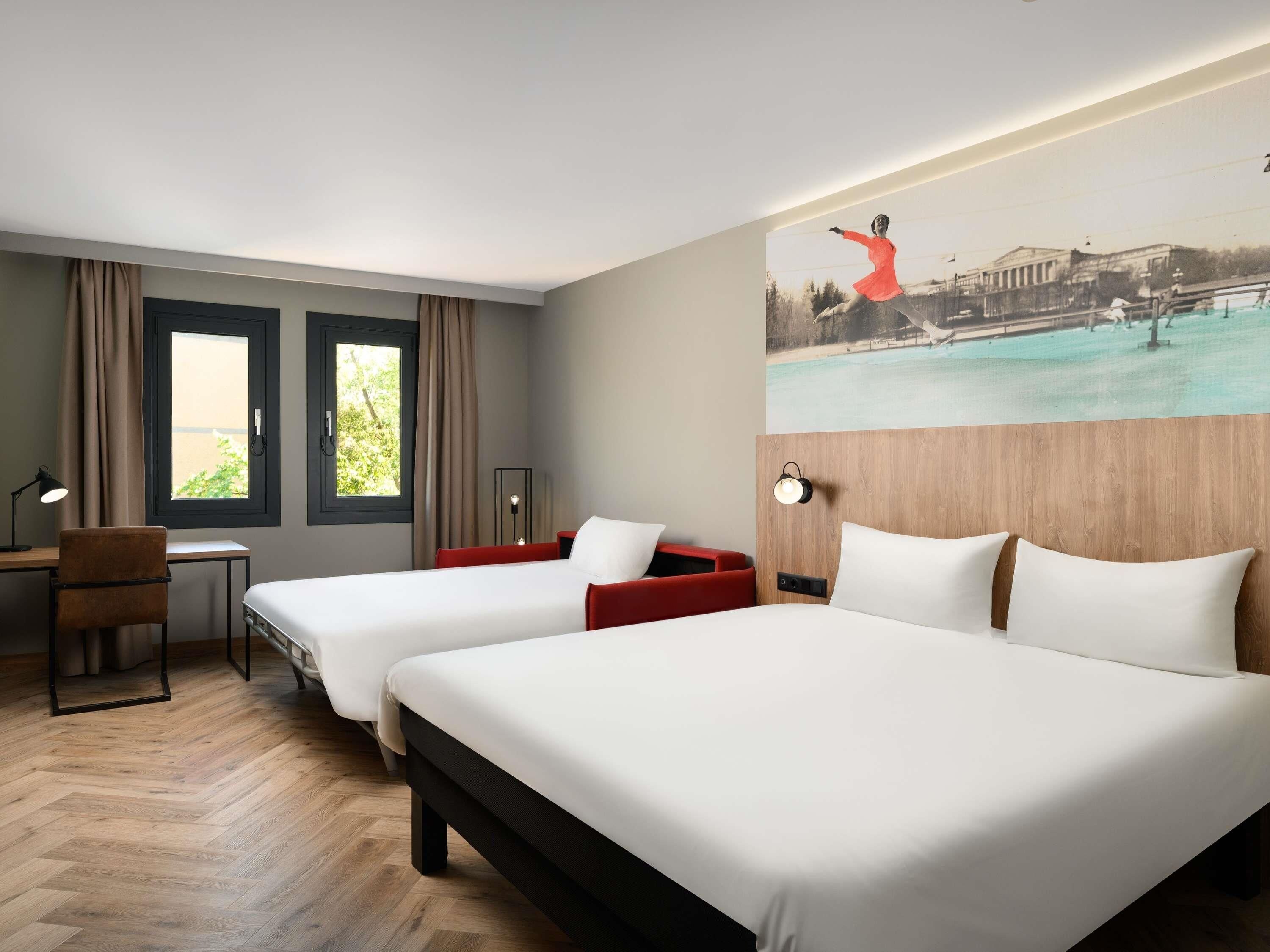 Habitación de hotel con dos camas, un escritorio, una silla, una lámpara y un cuadro en la pared.
