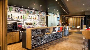 A modern bar area with a wooden counter, bar stools, and a wall with a black and white mural. - ibis Styles Budapest Heroes Square (Budapest)