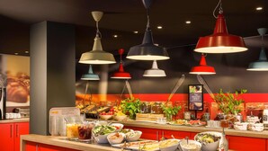 A buffet counter with various food items, a coffee machine, and hanging pendant lights. - ibis Styles Budapest Heroes Square (Budapest)