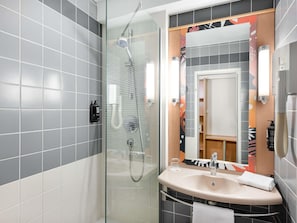 Un baño moderno con ducha de vidrio, lavabo con toalla y espejo con marco decorativo.