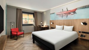 Ein Hotelzimmer mit einem großen Bett, einem roten Sessel, einem Schreibtisch und einem Bild eines Bootes an der Wand.