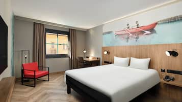 Habitación de hotel con una cama grande, una silla roja, un escritorio y un cuadro de un barco en la pared.