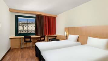 Een hotelkamer met twee bedden, een bureau, twee stoelen, een raam met gordijnen en uitzicht op een gebouw.