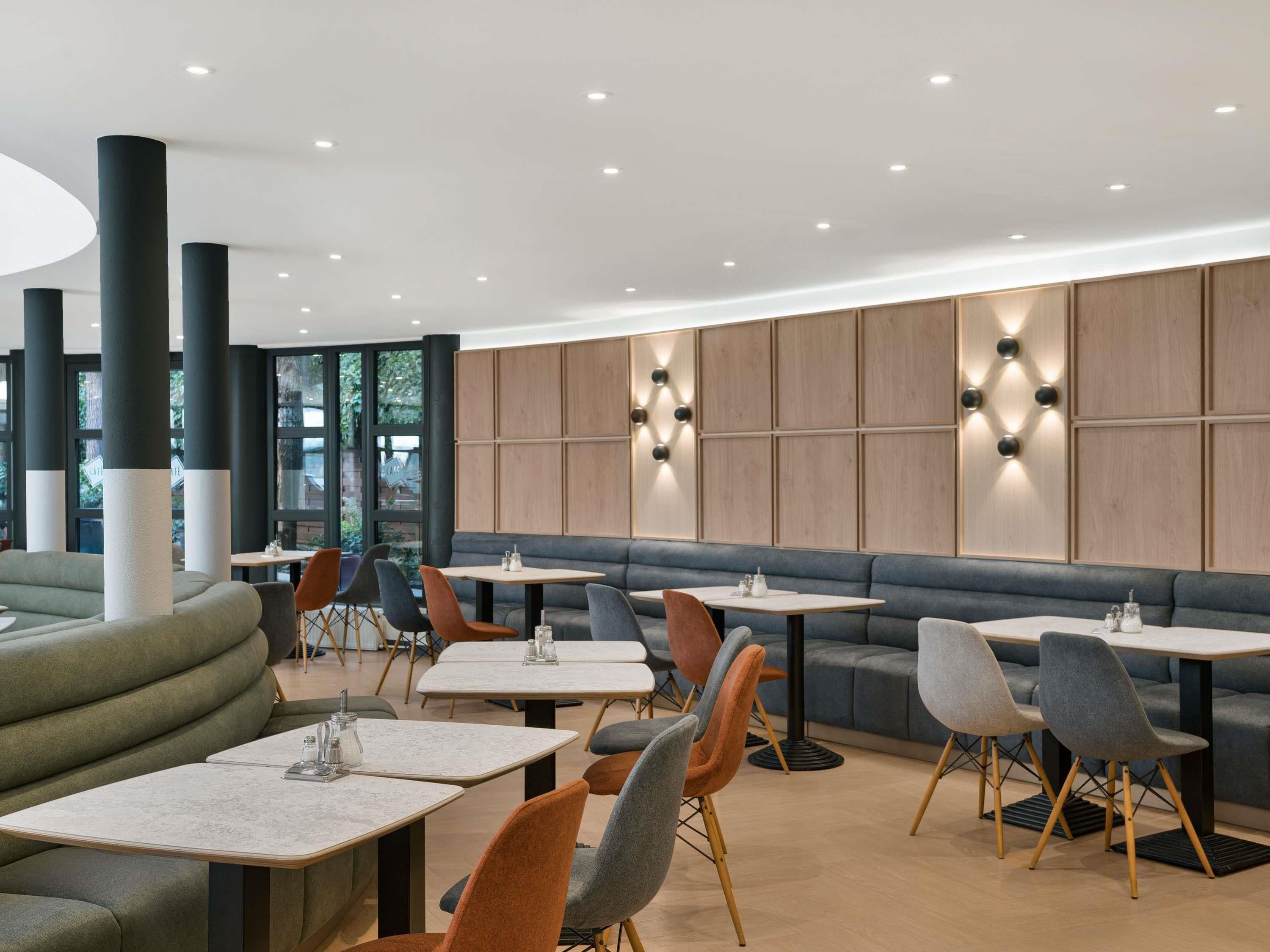 A modern interior with seating arrangements and tables, featuring a combination of sofas, chairs, and a high ceiling with recessed lighting.