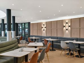 A modern interior with seating arrangements and tables, featuring a combination of sofas, chairs, and a high ceiling with recessed lighting.
