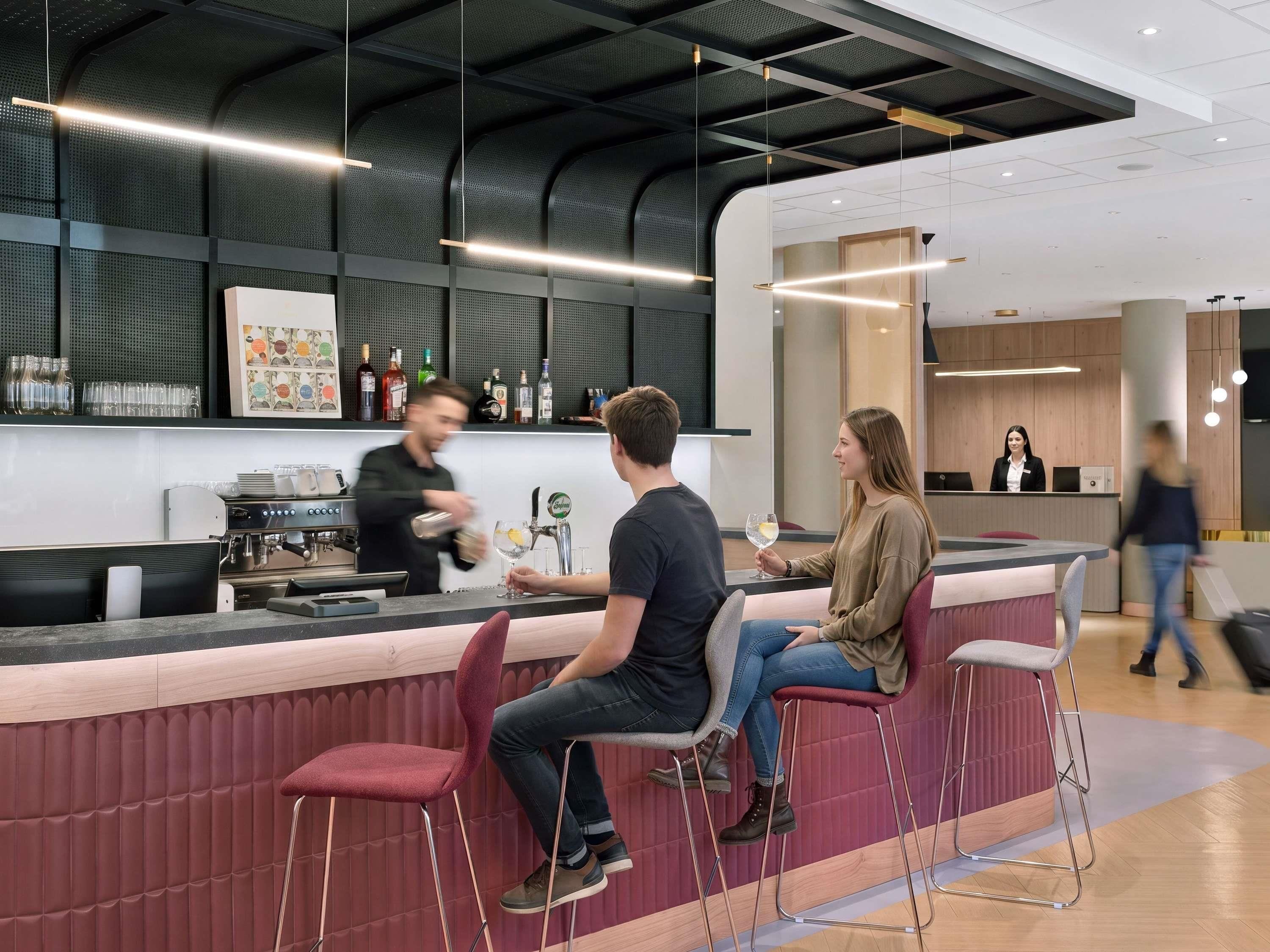 Eine moderne Bar mit einer Theke, Sitzgelegenheiten und einem Barkeeper, der Getränke zubereitet.