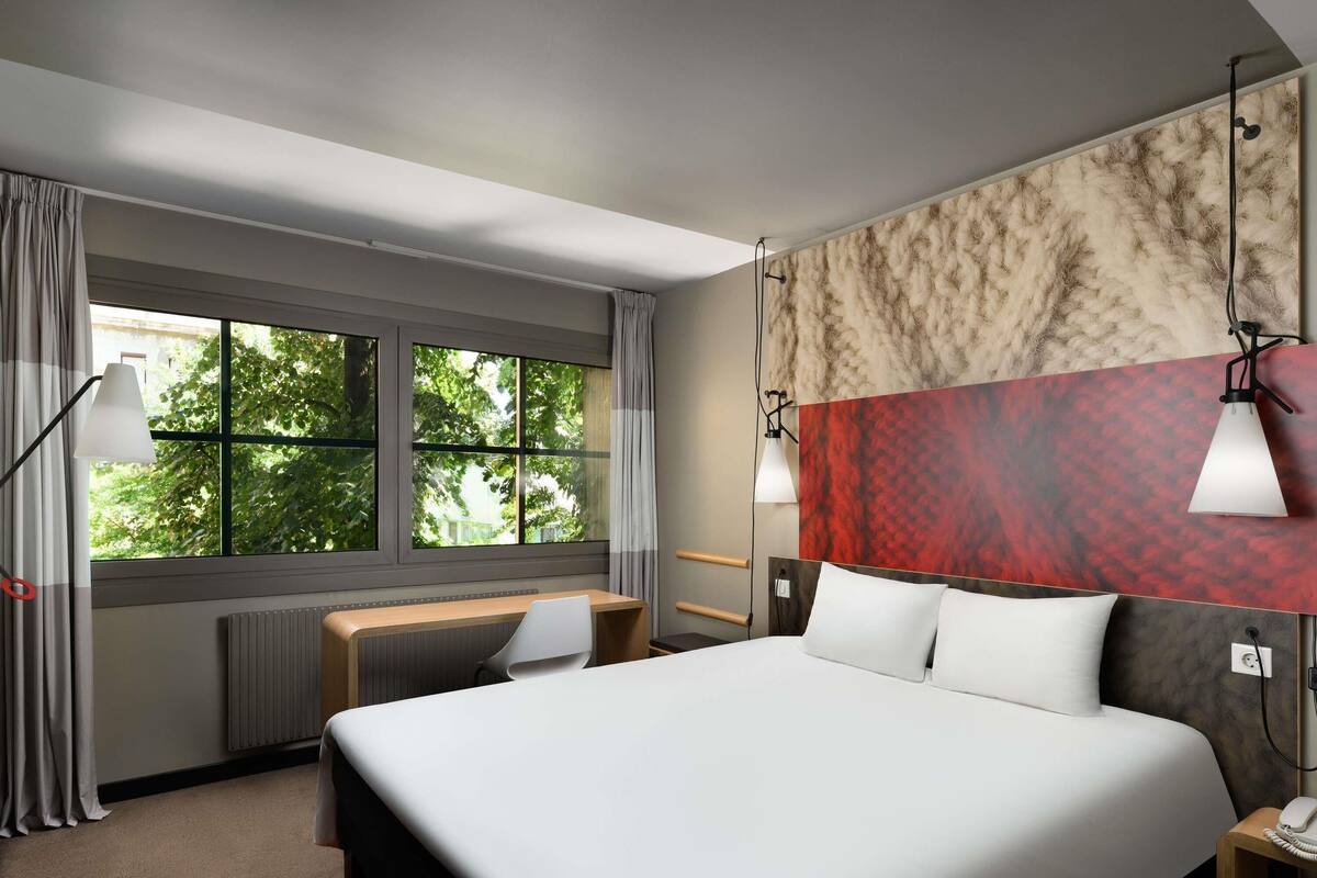Hotellihuone, jossa on sänky, työpöytä ja suuret ikkunat.