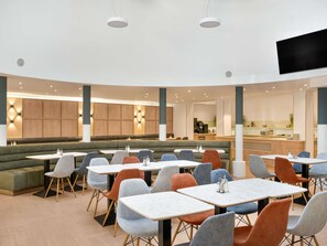 Un restaurante moderno con cabinas y mesas, una zona de cocina y un televisor de pantalla plana.