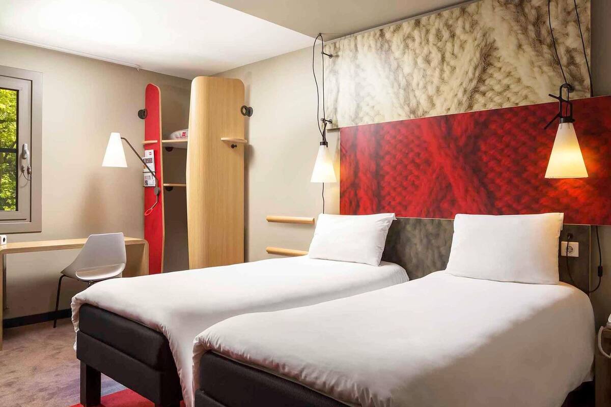 Hotellihuone, jossa on kaksi sänkyä, työpöytä, tuoli, vaatekaappi ja punainen matto.