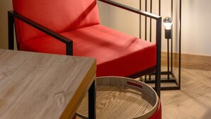 A red chair with a wooden table and a floor lamp. - ibis Styles Budapest Heroes Square (Budapest)