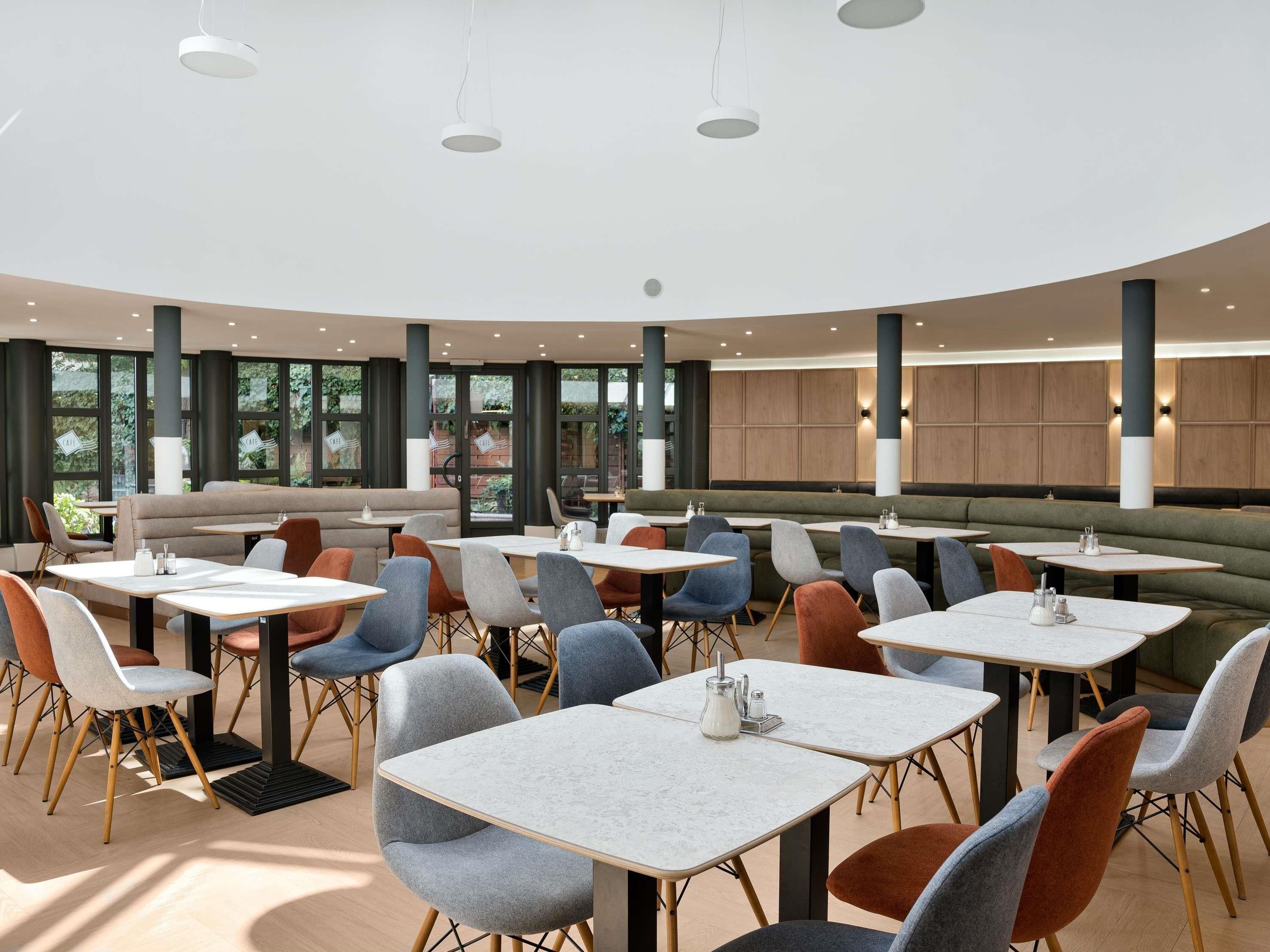 A modern dining area with round tables and chairs, large windows, and a curved ceiling.