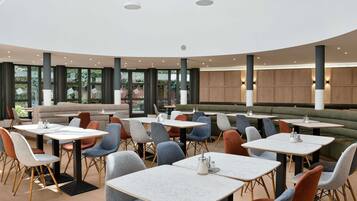 A modern dining area with round tables and chairs, large windows, and a curved ceiling.