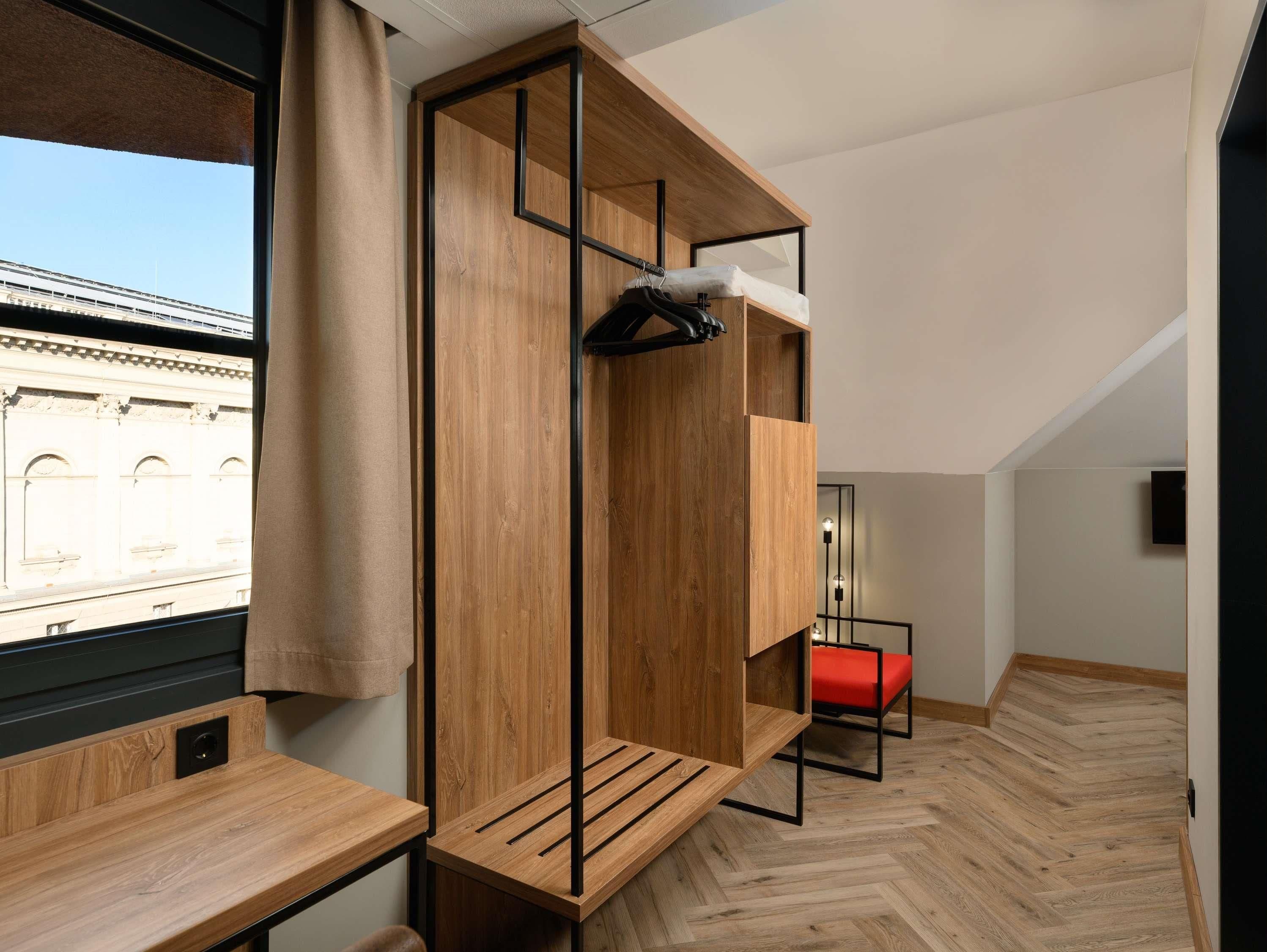 A modern, compact room with a wooden bunk bed, a small table, and a red chair.