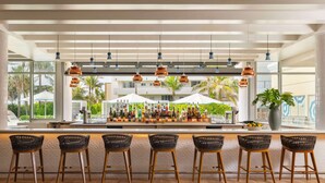 A bar area with a long counter, multiple bar stools, and a variety of bottles and glasses. - The Singer Oceanfront Resort, Curio Collection by Hilton (Singer Island)