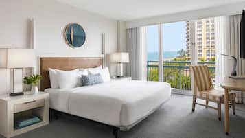 Une chambre d’hôtel avec un grand lit, deux tables de chevet avec des lampes, une vue sur l’océan et un balcon avec une chaise.